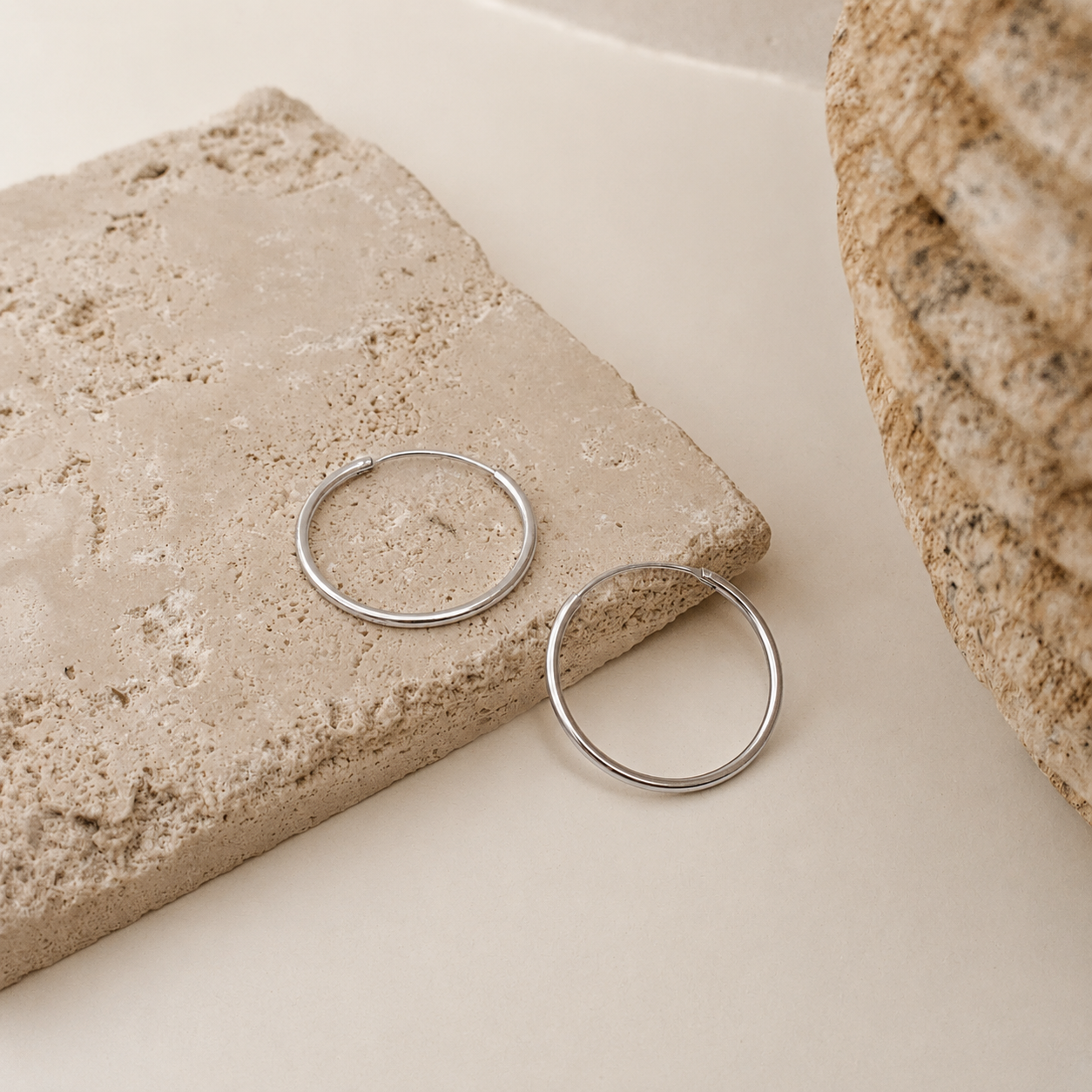 Silver hoop earrings on a stone surface with a neutral background